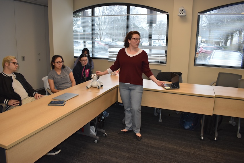 A woman in a red shirt stands in the middle of a classroom as students look on