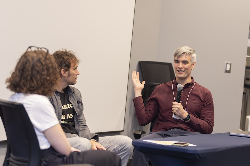 Man sits across from woman and another man holding a microphone at a conference