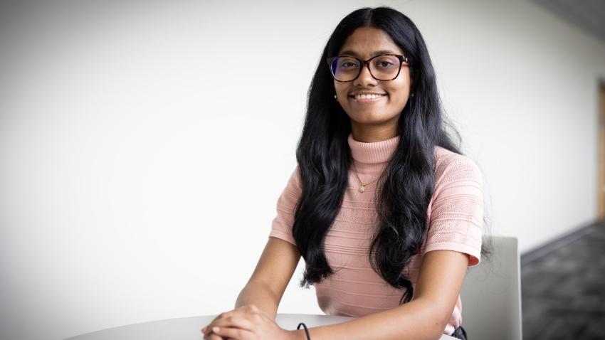 Woman wearing glasses and pink shirt sitting inside smiling