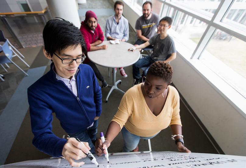 Male and female students working on white board togther