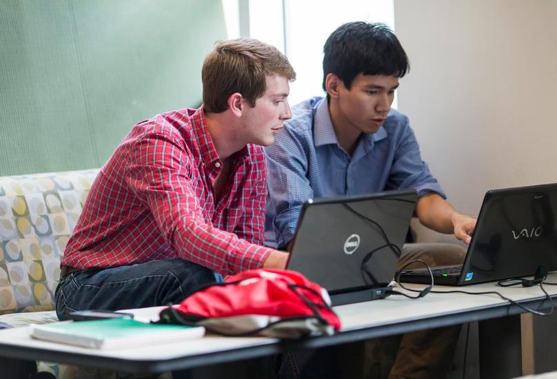 Two students looking at their laptops together.