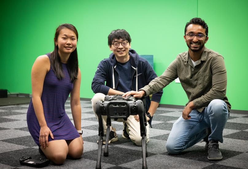 Three graduate students kneeling next to a robot.